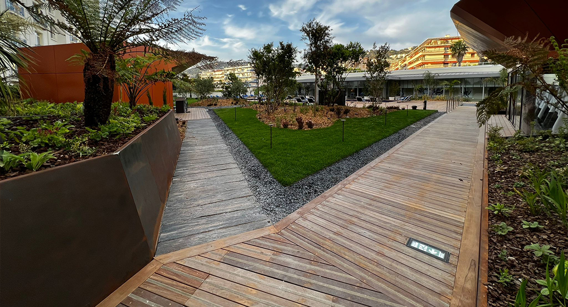 Aménagement extérieur d’hôtel avec grandes jardinières en acier Corten, cheminements en bois et espace paysager contemporain.