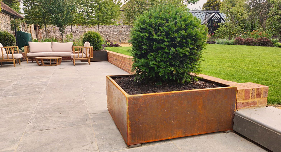Grande jardinière rectangulaire en acier Corten accueillant un arbuste sur la terrasse paysagée d’une villa.