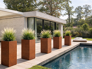 Jardinière Corten carrée haute plantée de graminées pour encadrer l’entrée d’un bâtiment contemporain.