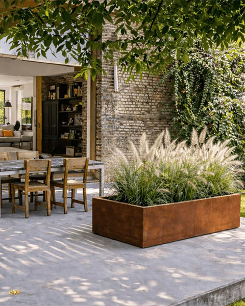 Jardinière rectangulaire en acier Corten accueillant des graminées sur la terrasse d’une maison contemporaine.