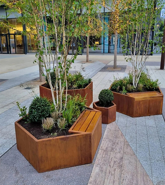 Jardinières en acier Corten avec assises en bois intégrées dans un espace extérieur d’hôtel ou de restaurant.
