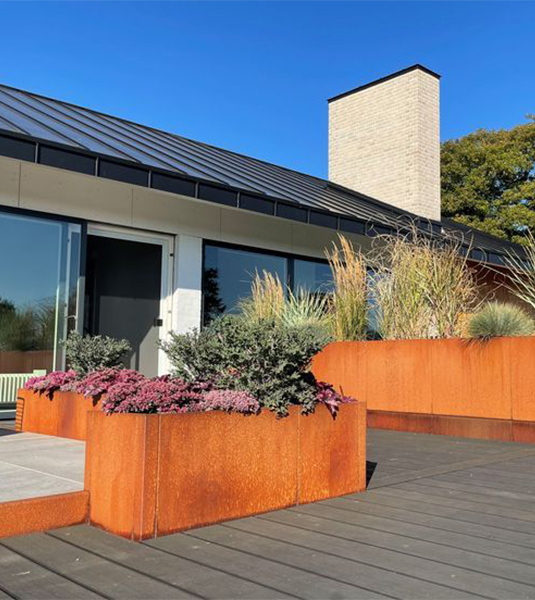 Jardinières rectangulaires en acier Corten plantées de graminées et de fleurs sur la terrasse d’une villa moderne.